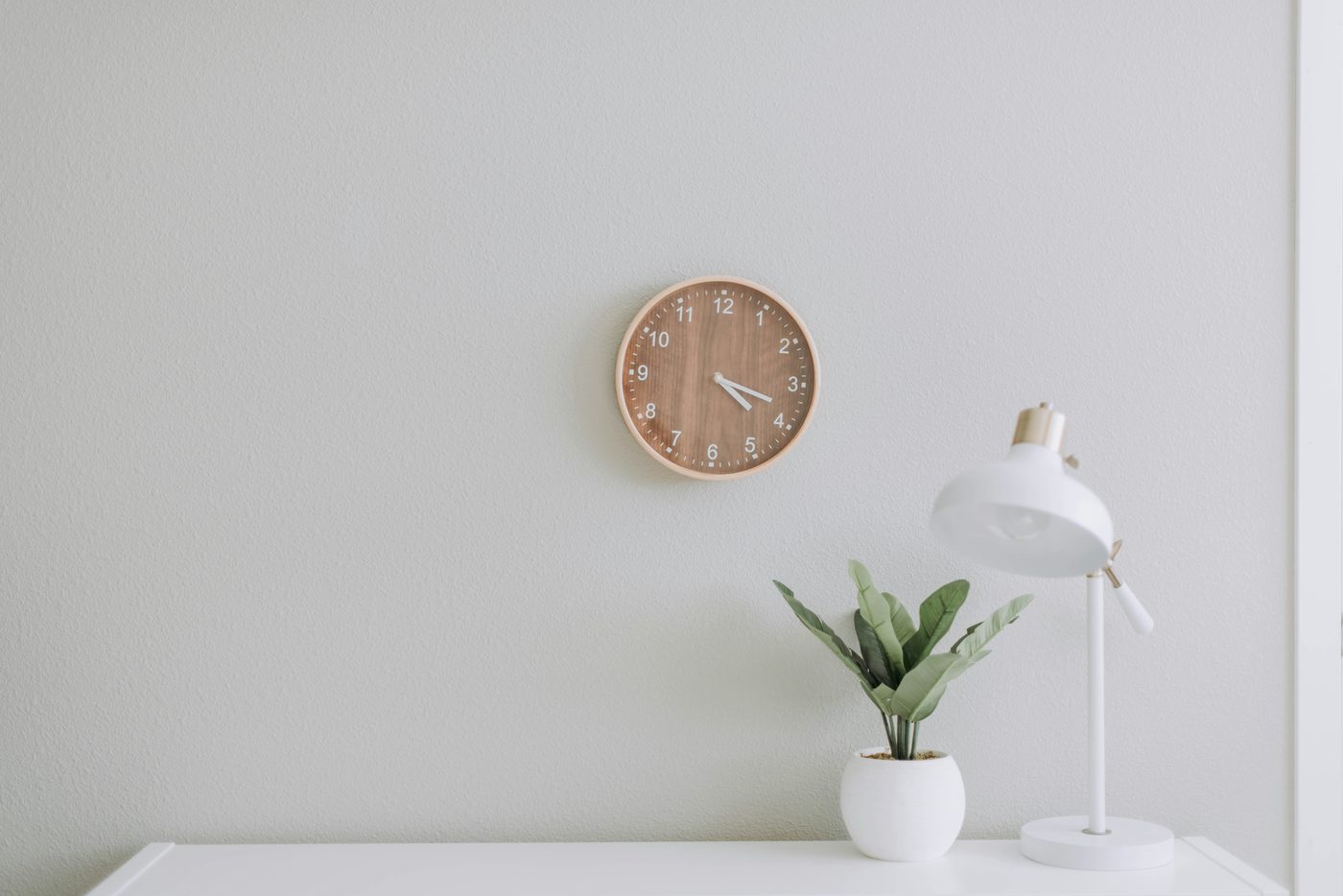 A calm, minimal home corner with a lamp, a small plant, and a wooden clock