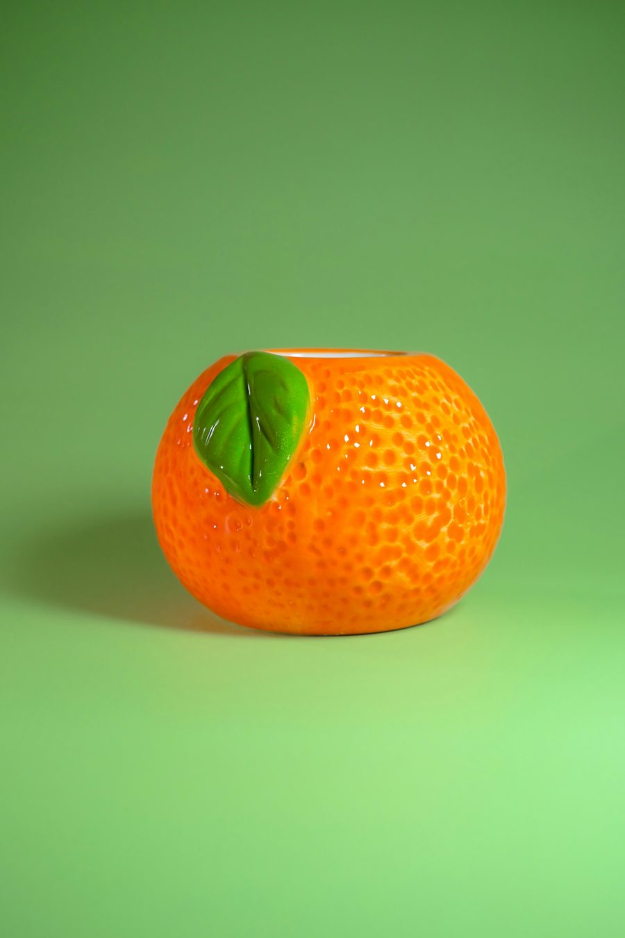 A round, glossy ceramic vessel shaped like an orange, with a green leaf accent