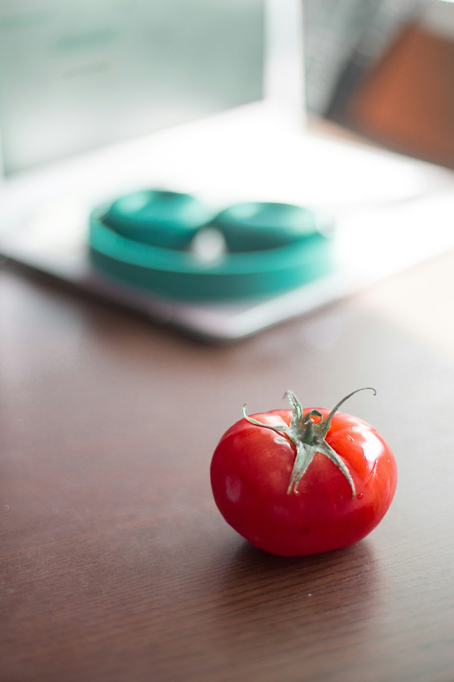 A single ripe tomato on a wooden table, representing the shape and colour of the upcoming lamp